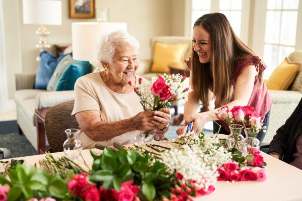 A resident sitting with a younger woman arranging a bouquet.