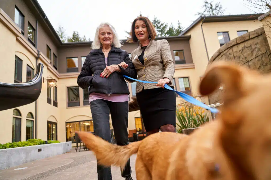 Two women walking dog at senior living facility.