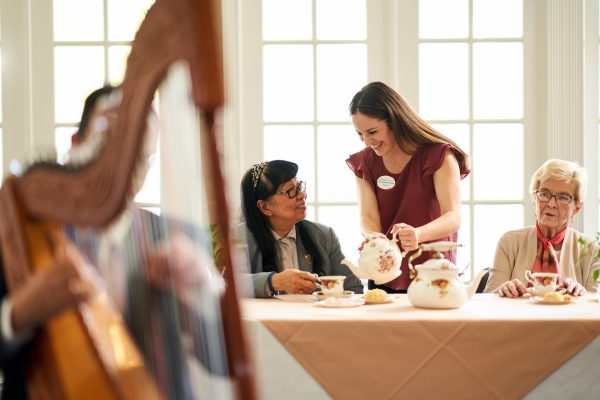 Residents sitting, drinking tea, with a harpist playing in the foreground