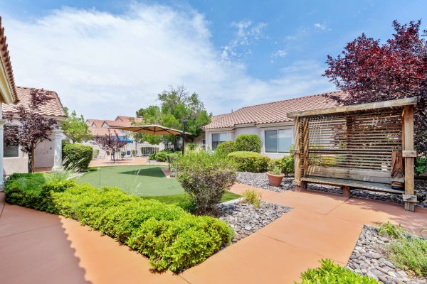 A view of the outside of Aegis Living, with a walking path, shrubs, and the mini-putt course in the background