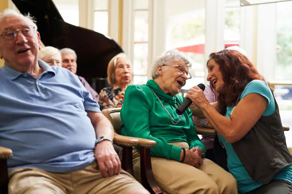 Elderly woman singing with microphone in assisted living home.