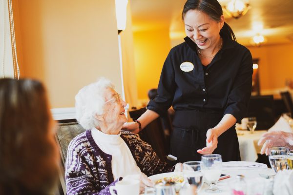 A resident sitting at a table, eating, talking to an employee