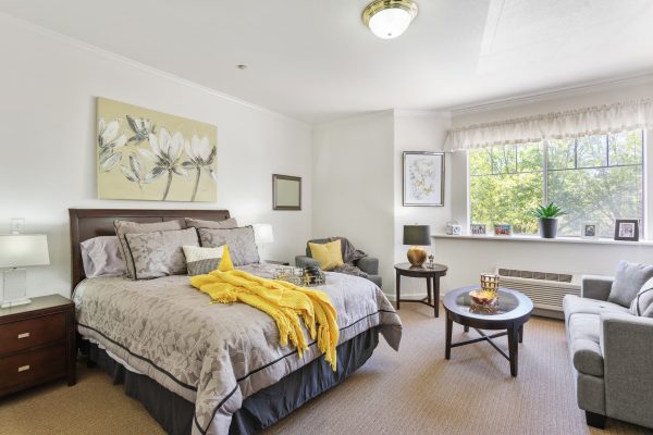 A bedroom with a cozy bed, a large window, armchairs, and small coffee tables