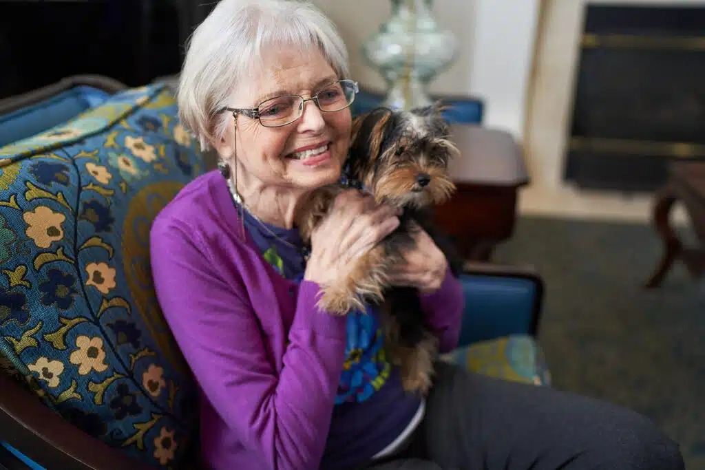 Elderly woman smiling with small dog indoors.