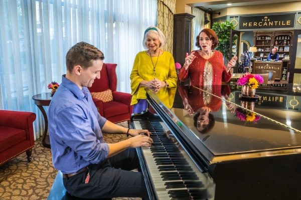 An employee playing the piano while two residents watch and sing