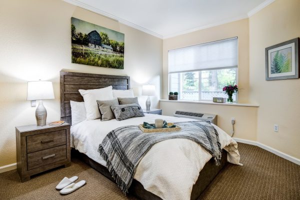 A bedroom with a cozy bed, a large window, and nightstands on either side of the bed.