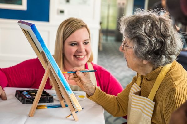 A resident painting a picture and sitting beside a young lady