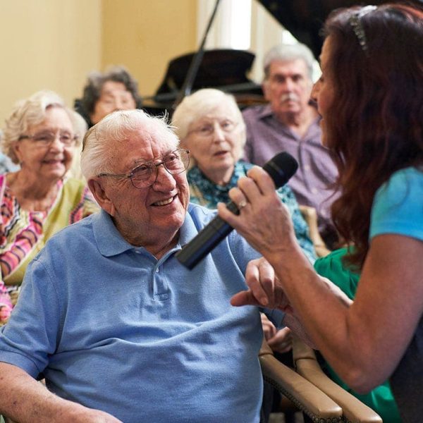 A woman holding a microphone speaking to a group of residents, who are smiling at her