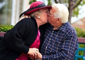 A elderly couple kissing outside on a bench