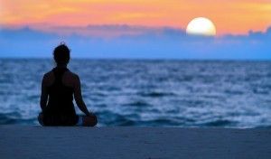 Silhouette of person meditating at sunset on a beach.