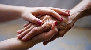 Closeup of younger woman's hands clasping elderly person's hand