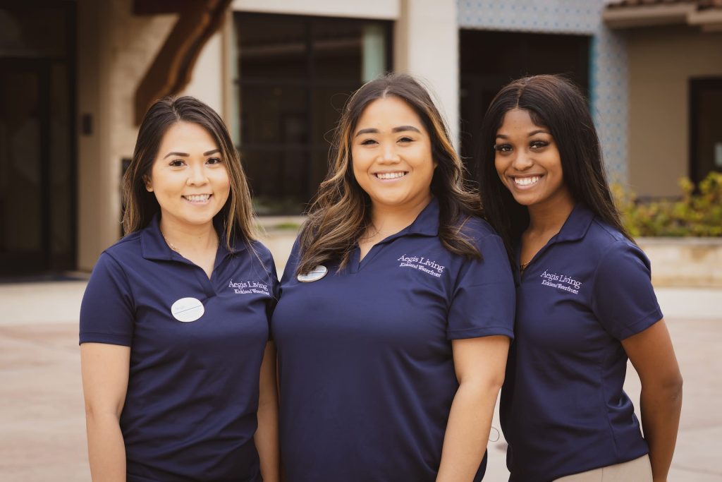 Three Aegis Living employees standing, smiling at the camera