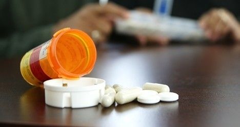 a prescription bottle opened on table with pills pilling out.