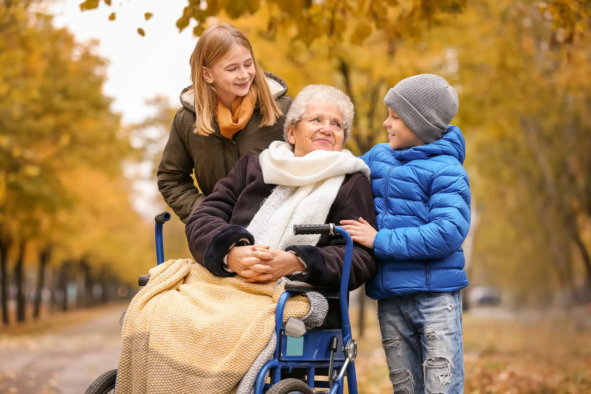 Grandmother in wheelchair with grandchildren in autumn park.