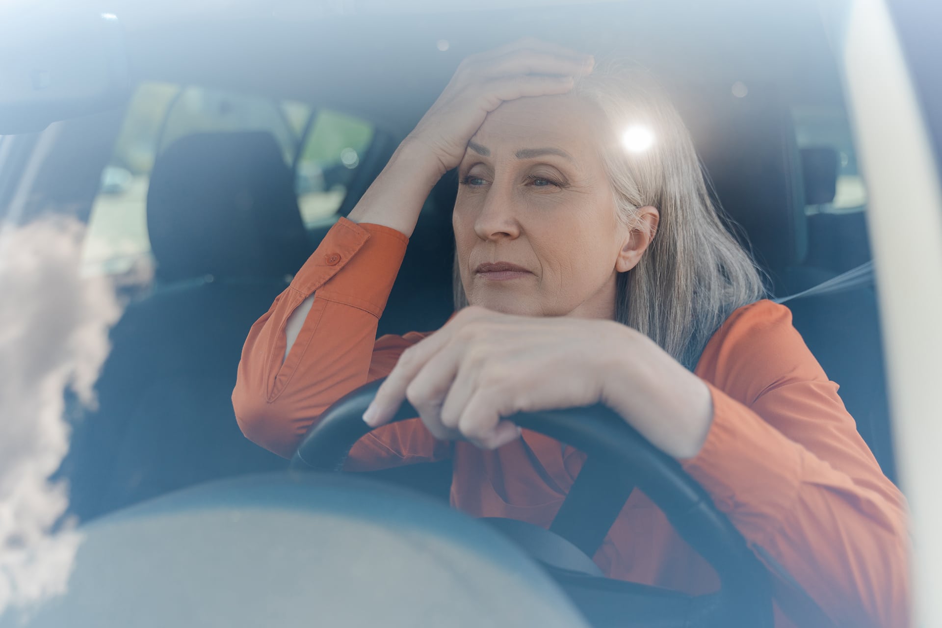 Tired woman sitting in a car, hand on head.