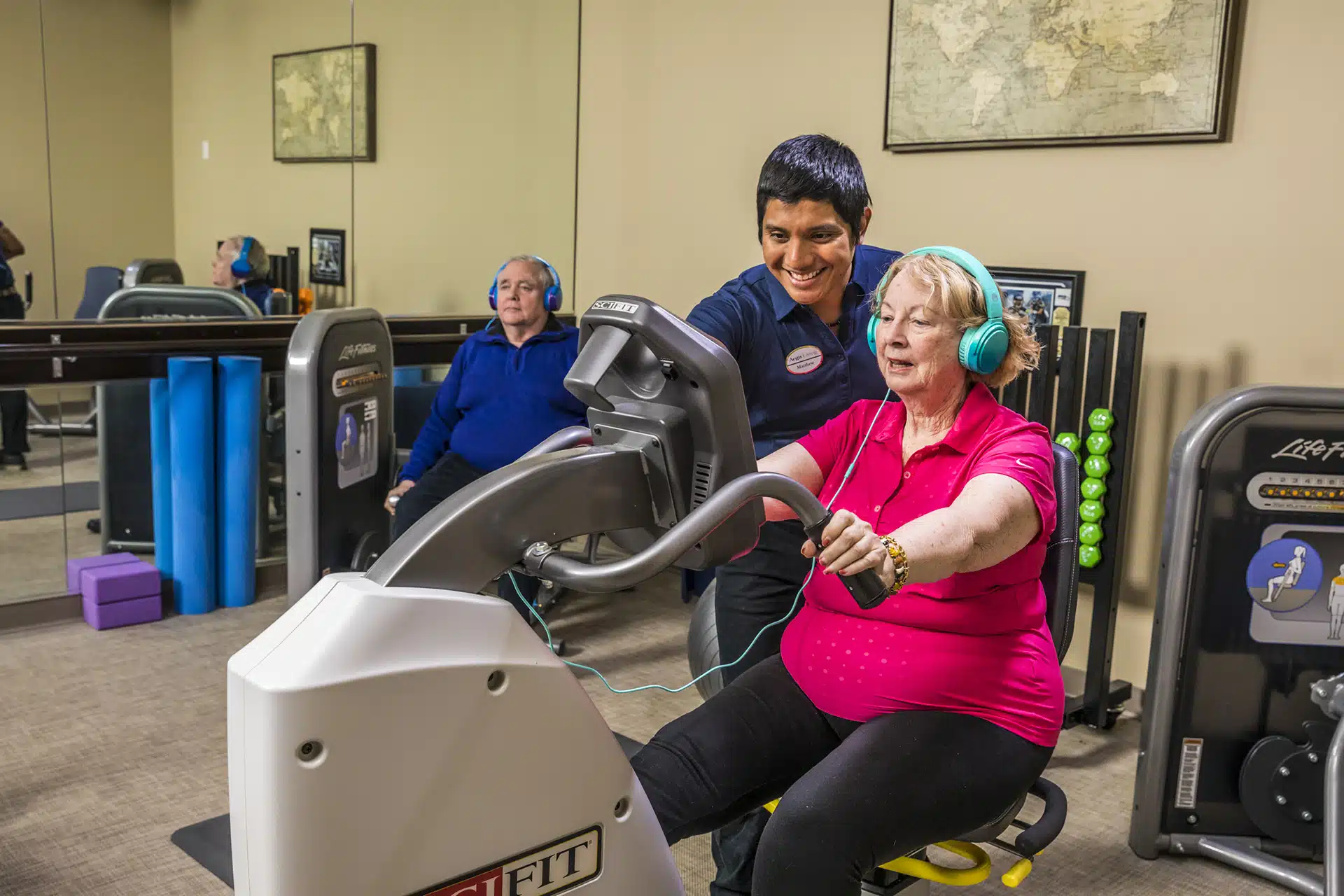 Trainer assists elderly woman on exercise bike.