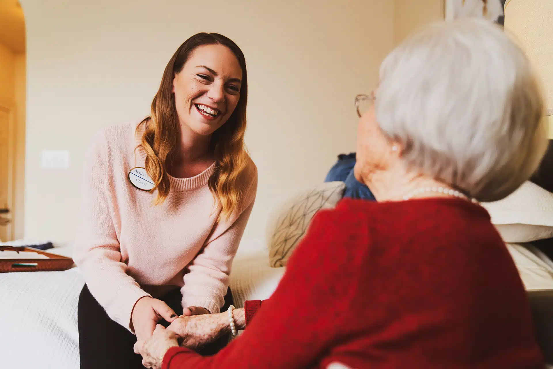 Caregiver smiling and holding elderly woman's hands.
