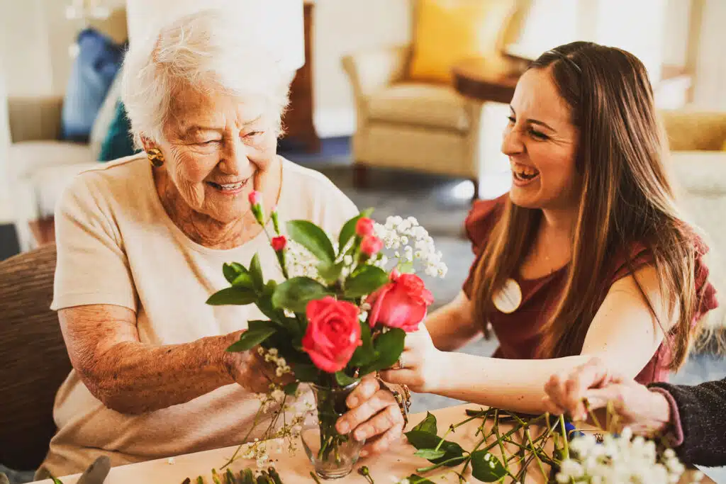 Smiling women arranging flowers together joyfully.